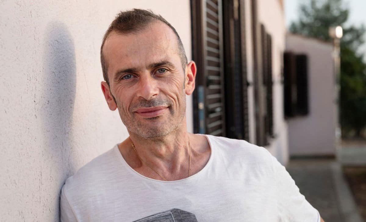 Photo portrait d'Andrea devant sa maison. Andrea vit avec la sclérose en plaques et aurait aimé en savoir un peu plus sur ce à quoi s'attendre en termes de problèmes vésicaux et intestinaux associés.  