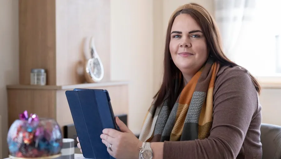 Photo de Sarah assise à une table. C'est quatre ans après son diagnostic initial que Sarah a fait le lien entre ses problèmes de vessie et sa sclérose en plaques. 